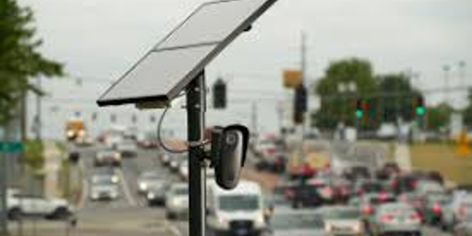 A solar-powered license plate reader camera on a pole overlooking a busy multi-lane road