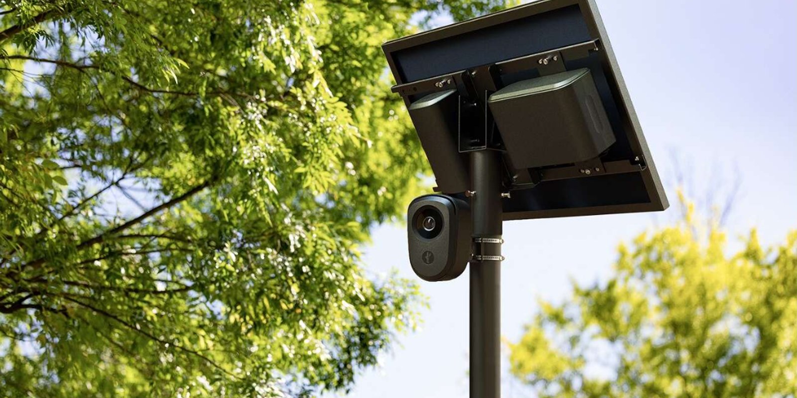 A solar-powered automated license plate reader camera mounted on a pole among green trees